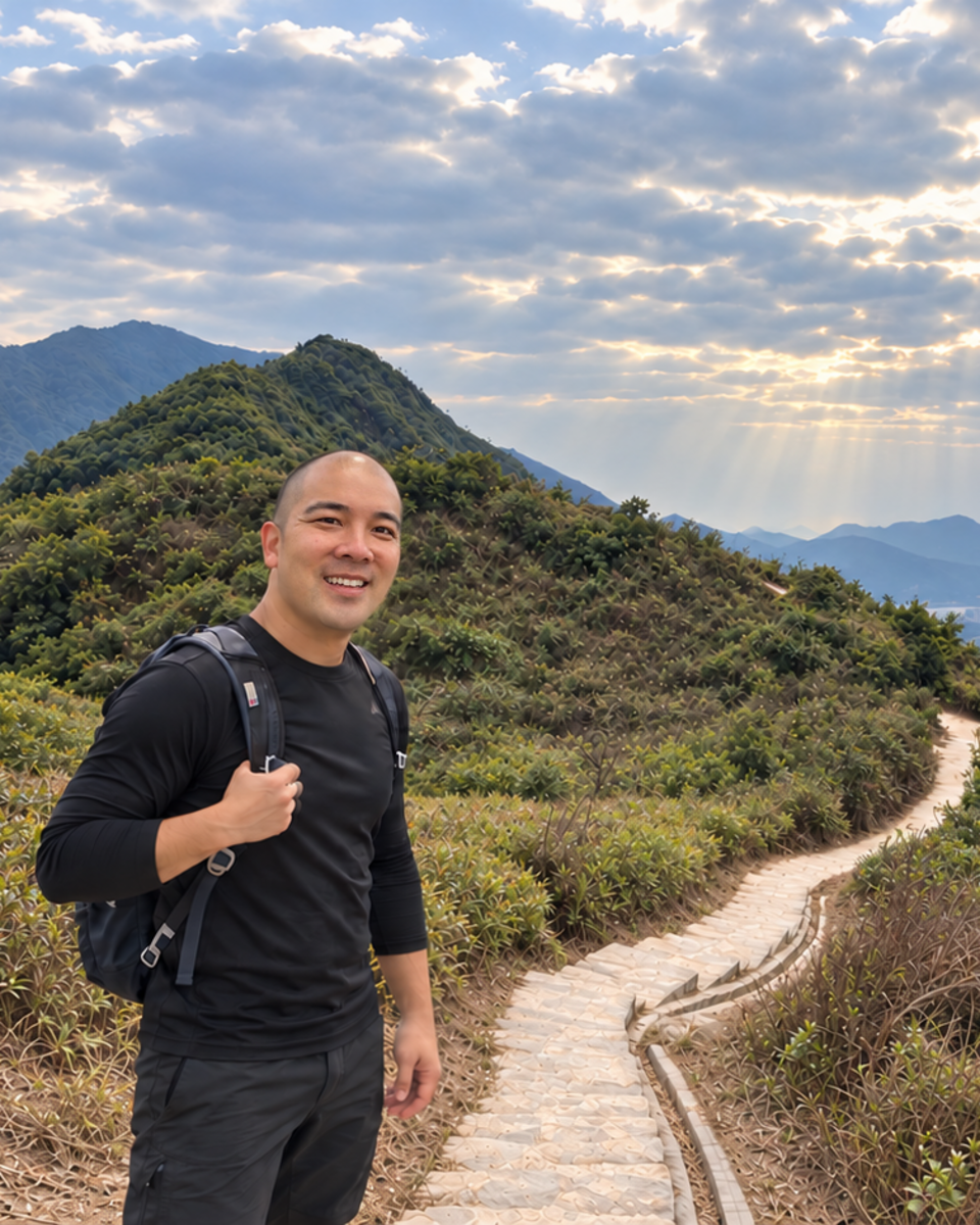 Norbert Woo smiling on a winding stone hiking trail above the hills and sea of Hong Kong